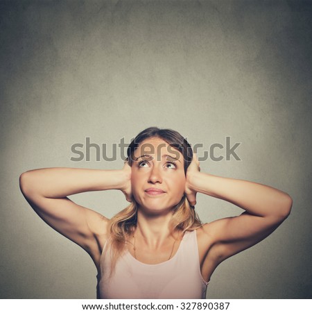 angry unhappy stressed woman covering her ears looking up stop making loud noise it\'s giving me headache isolated on grey wall background. Negative emotion face expression feeling