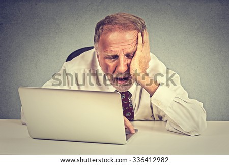 Too much work to do. Tired sleepy senior man sitting at his desk in front of laptop computer isolated on grey wall office background. Busy schedule in college, work place, sleep deprivation concept