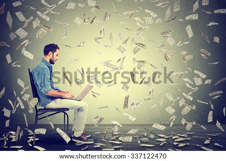 Young man using a laptop building online business making money dollar bills cash falling down. Money rain beginner IT entrepreneur success economy concept