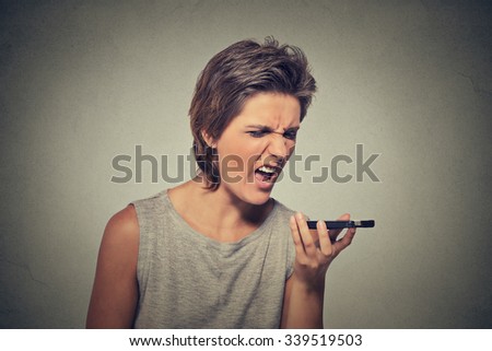 Portrait angry young woman screaming on mobile phone isolated on gray wall background. Negative emotions feelings