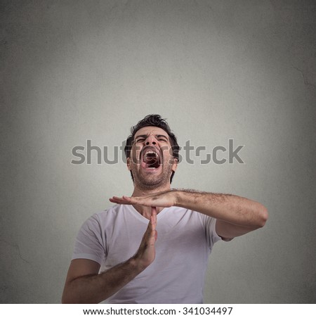 Young man showing time out hand gesture, frustrated screaming to stop isolated on gray wall background. Too many things to do. Human emotions face expression reaction
