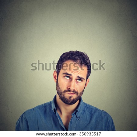 Portrait closeup funny confused skeptical man thinking looking up isolated on gray wall background with copy space above head. Human face expressions, emotions, feelings, body language