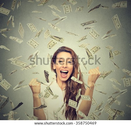 Portrait happy woman exults pumping fists ecstatic celebrates success under a money rain falling down dollar bills banknotes isolated on gray wall background with copy space