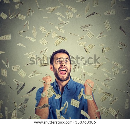 Portrait happy man exults pumping fists ecstatic celebrates success screaming under money rain falling down dollar bills banknotes isolated gray background with copy space. Financial freedom concept