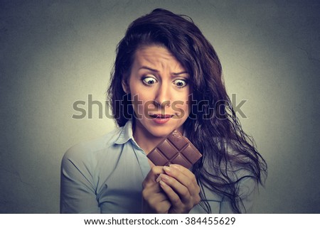 Portrait sad young woman tired of diet restrictions craving sweets chocolate isolated on gray wall background. Human face expression emotion. Nutrition concept. Feelings of guilt. Funny looking girl