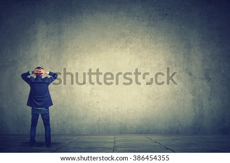 Rear view of business man standing in front of a wall hands on head wondering what to do next. Full length of businessman facing the wall