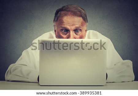 Closeup portrait elderly surprised man sitting at table working on laptop computer looking carefully at screen isolated on gray office wall background