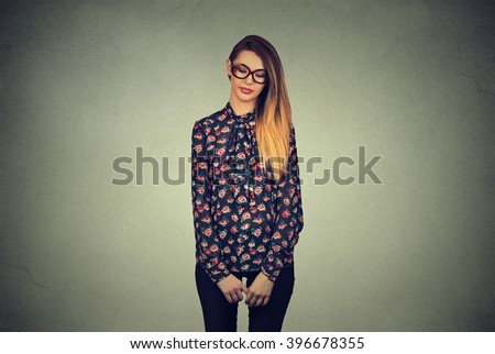 Sad shy insecure young woman in glasses looking down avoiding eye contact standing isolated on gray wall background