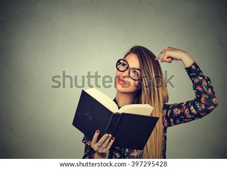 Portrait young woman with glasses, holding, reading book, scratching head, looking up confused, isolated on gray wall background with copy space. Face expression, emotions, reaction