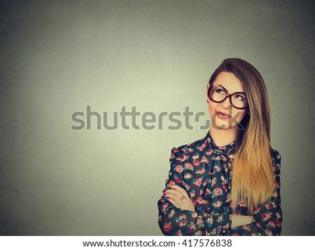 Portrait closeup funny confused young skeptical woman in glasses thinking looking up isolated on gray wall background copy space above head. Human expressions, emotions, feelings, body language