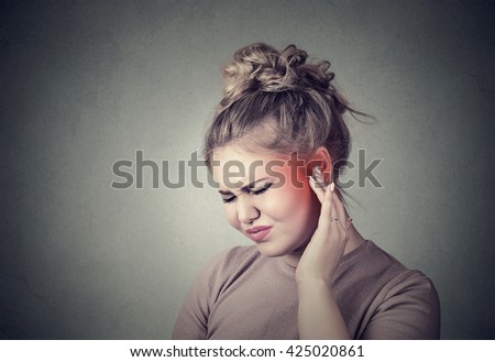 Tinnitus. Closeup up side profile sick female having ear pain touching her painful head colored in red isolated on gray background
