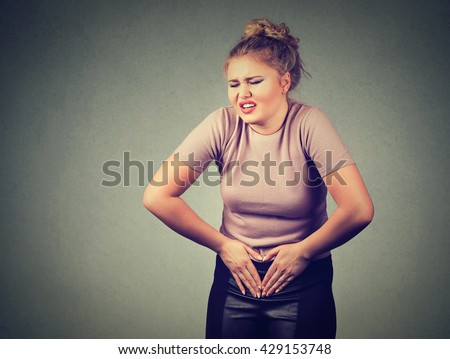 Portrait young woman hands on stomach having bad aches pain isolated on gray wall background. Food poisoning, influenza, cramps. Negative emotion face expression reaction health issues problems