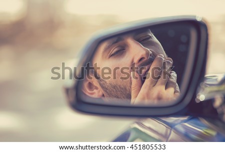 Side mirror view reflection sleepy tired fatigued yawning exhausted young man driving his car in traffic after long hour drive. Transportation sleep deprivation accident concept