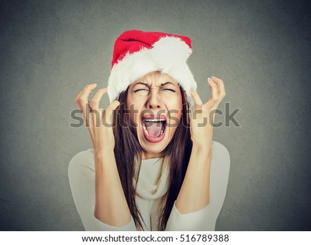 Closeup portrait of worried stressed overwhelmed young woman wearing red santa claus hat, screaming going crazy, isolated on gray background. Emotion facial expression. Last minute christmas shopping