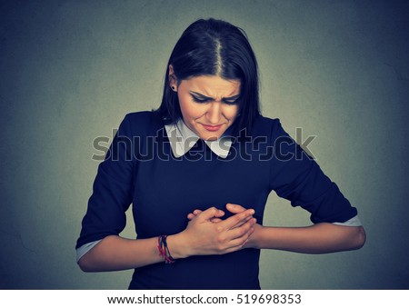 sick woman with heart attack, pain, health problem holding touching her chest with hands isolated on gray wall background. Human face expression