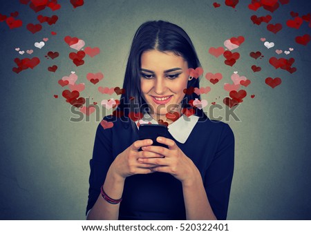 Portrait happy woman sending love sms text message on mobile phone with red hearts flying away from screen isolated on gray wall background. Human emotions feelings