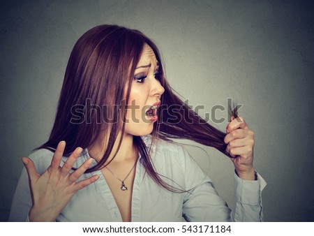 Unhappy upset frustrated young woman surprised she is losing hair, noticed split ends. Gray background. Human face expression emotion. Beauty hairstyle concept