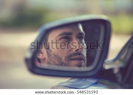 Side mirror reflection of a young man driving his new car. Safe trip journey driving concept