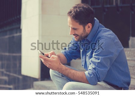 Man texting on phone. Casual urban professional entrepreneur using smartphone smiling happy outside office building. Outdoor portrait of modern young guy with mobile in the street sitting on stairs