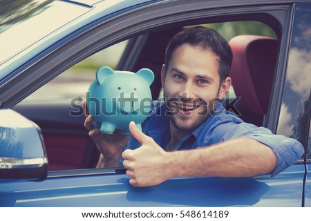 Happy man sitting inside his new car holding piggy bank showing thumbs up