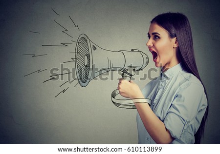 Young woman screaming in megaphone isolated on gray wall background. Negative face expression emotion feelings. Breaking news, power, social media communication concept