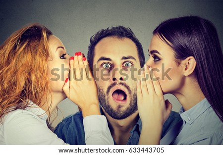 Two young women telling whispering secret gossip in the ear to an amazed shocked man with wide open mouth. Human emotions face expression reaction. Hot news concept
