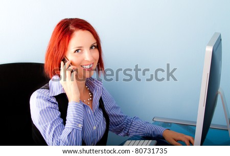 Office girl busy working on desktop computer, speaking on mobile phone, smiling