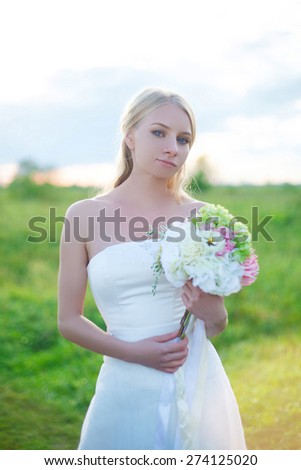 Unhappy blond bride standing in a field looking at the camera and gets angry. Funny face. Beautiful bride. Wedding Day. Beautiful Happy woman
