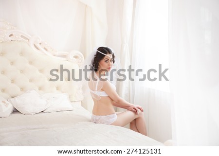 Beautiful bride in underclothes sitting on a bed near the window. Bride getting ready on her wedding day