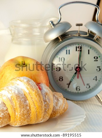 Croissant with jam and a jug of milk and an alarm clock, a light morning meal