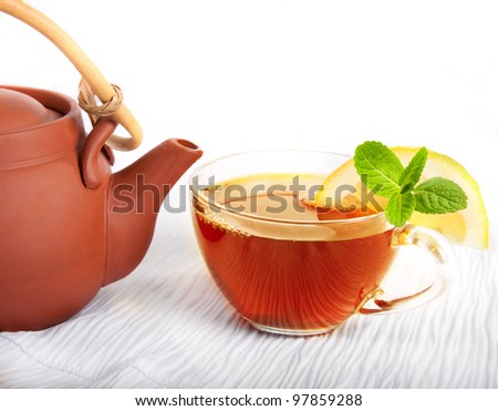 Cup of fragrant tea flowing from a ceramic teapot