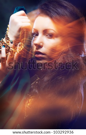 Portrait of irresistible gypsy woman with golden jewelleries in low key, mixed light, low shutter speed.