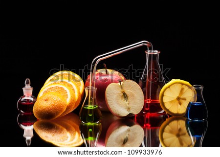 Still life of laboratory glassware with colorful liquids and fruits on black background
