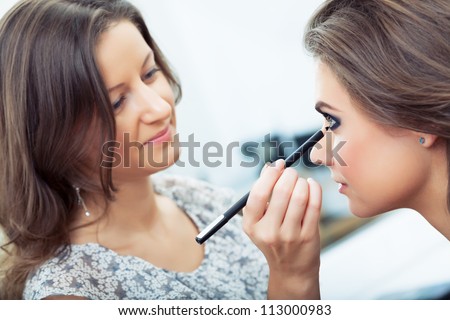 Make-up artist applying eyeliner on model\'s lower lid, selective focus on model, close up