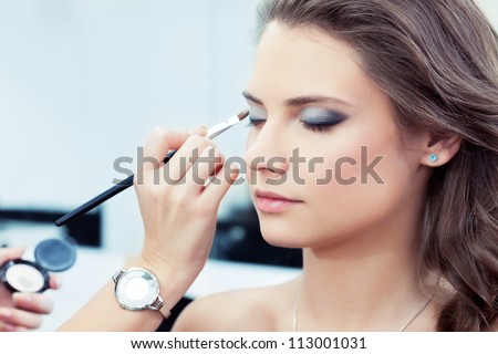 Make-up artist applying bright base color eyeshadow on model's eye and holding a shell with eyeshadow on background close up Make-up artist applying bright base color eyeshadow on model's eye and holding a shell with eyeshadow on background close up