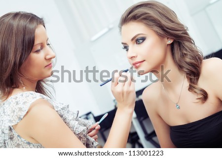 Make-up artist applying lipstick with a brush on model\'s lips