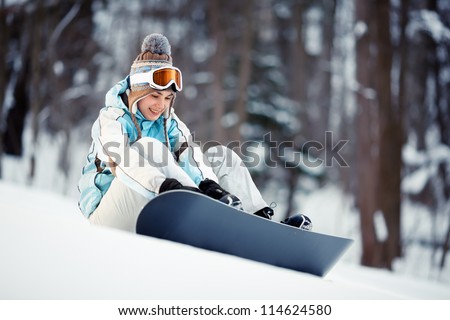 Young beautiful woman strapping on her snowboard at ski slope