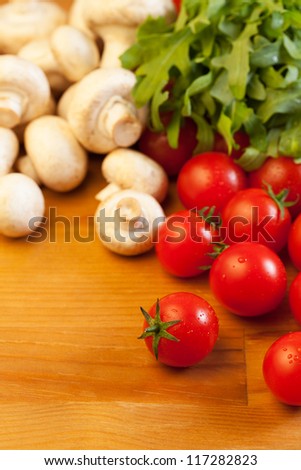 Tomatoes, mushrooms and rocket salad on wooden table, focus on foreground