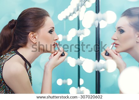 Young woman applying lipstick in front of a mirror