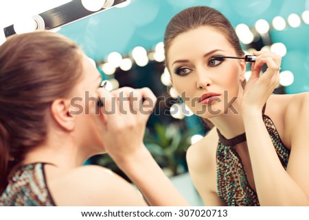 Young woman applying mascara, focus on the reflection in the mirror