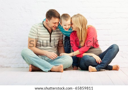 Happy family of three sitting on the floor near the wall and laughing:  mother, father and little boy. Mother is pregnant.