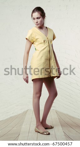 Young woman in short yellow dress standing behind white wall on wooden floor, distorted space