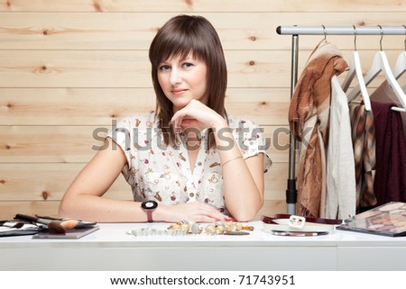 Woman\'s stylist with attributes of her work, standing near coat rack with clothes, cosmetics and accessories on the table.