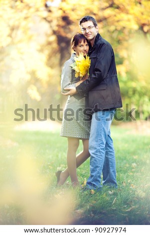 Lovers spend sunny day in the autumn park, they hold a bouquet of autumn leaves; blurs around them