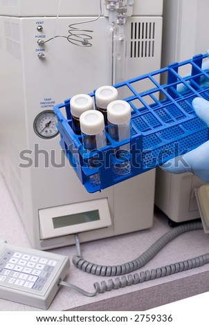 Lab vials,bottles and caps in a rack with out of focus research equipment in the background
