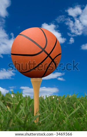 Basketball on golf tee from the ground level with grass and cloudy sky
