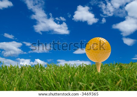 Yellow Golf ball close-up from the ground level with grass and cloudy sky