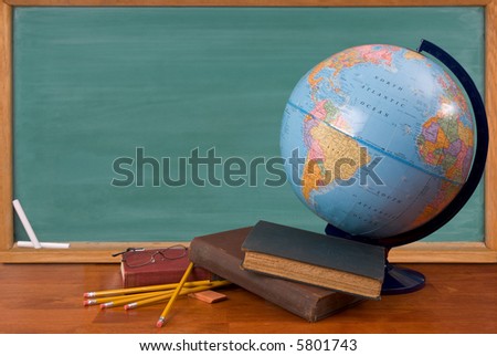 Old school books on a desk with a globe in front of a green chalkboard