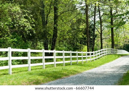 Long, private, country road along a white picket fence.
