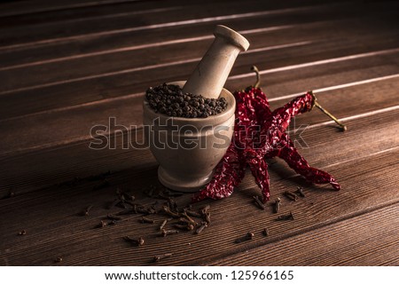 marble mortar with spices black pepper, carnation and red hot pepper on a wooden table